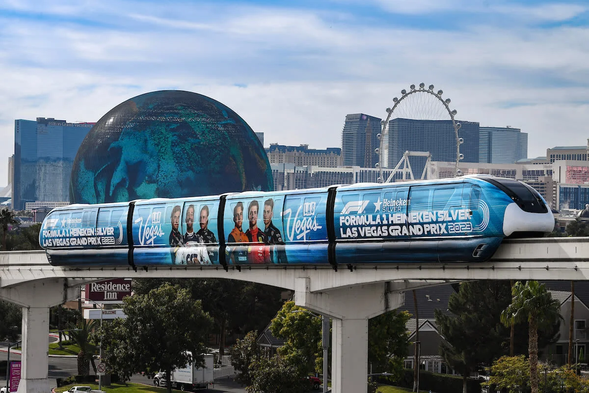 The accessible Las Vegas Monorail, wrapped in F1 Grand Prix advertising, passing by the Sphere and High Roller Ferris wheel, showcasing easy accessible travel in Las Vegas.