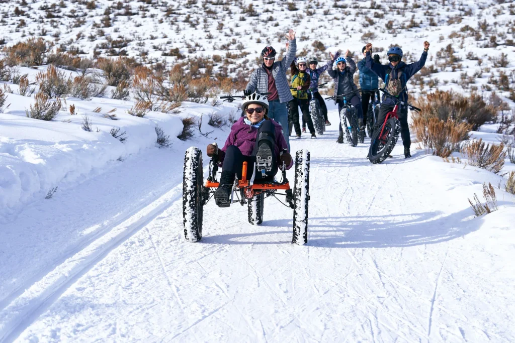 A smiling woman riding a recumbent adaptive fat-tire trike on a snowy trail at the National Ability Centre, showcasing active adventure options for accessible winter travel.